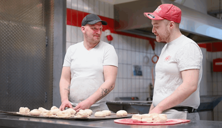 Auf dem Bild ist zu sehen wie dem Auszubildenden die Zubereitung der Campingbrötchen von Hand erklärt wird.